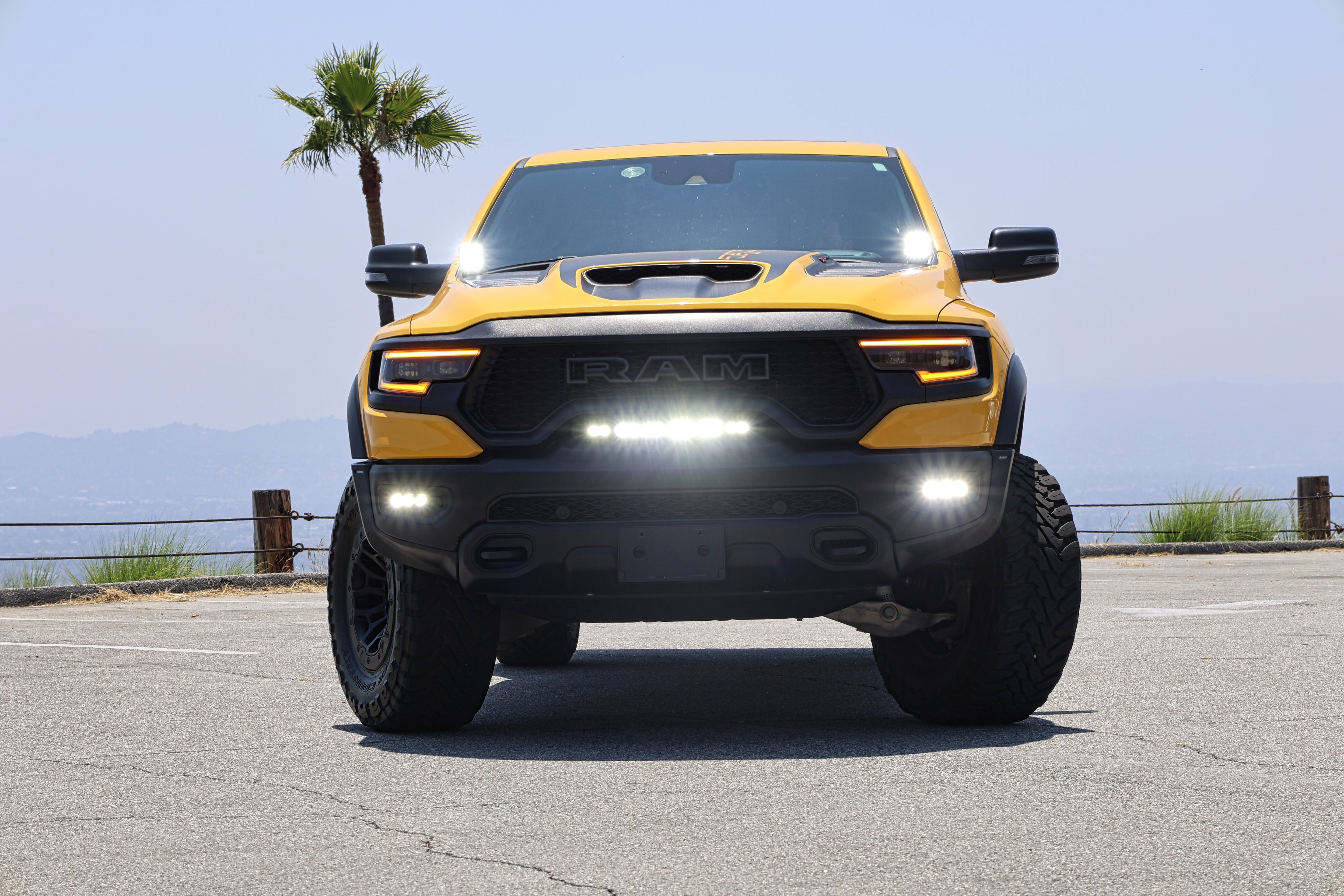 Yellow 2021-2024 RAM 1500 TRX with LED light bar installed on the front bumper, parked oceanside near palm trees