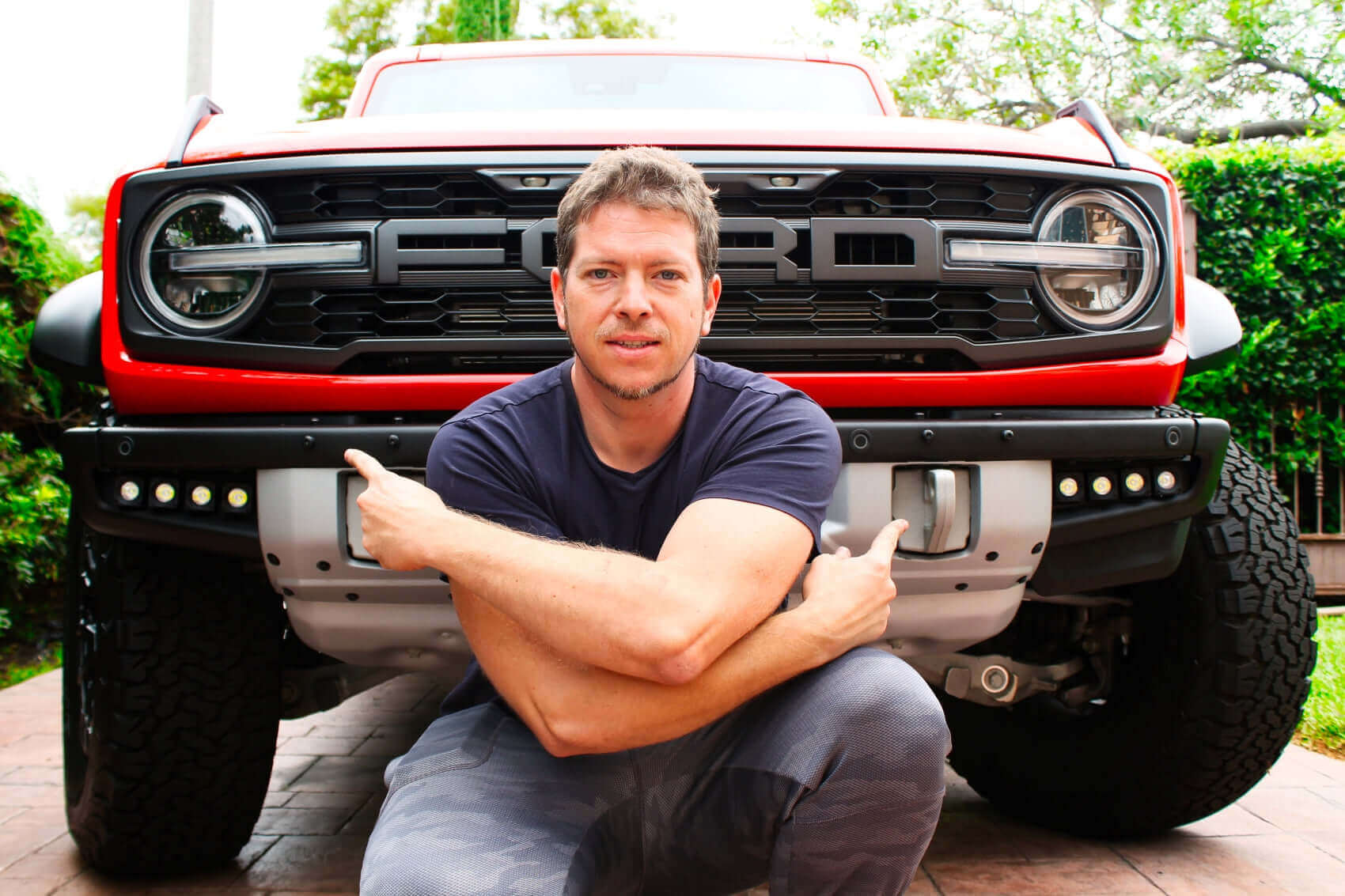 Start of Ford Bronco Raptor Design: man crouching in front of red Ford Bronco Raptor vehicle, showcasing front grille and rugged bumper