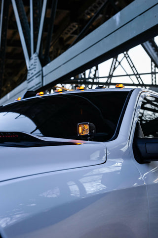 Alt Tag: 2025+ RAM 2500 3500 Ditch Lights with dual color amber DRL glowing on white heavy duty truck under bridge