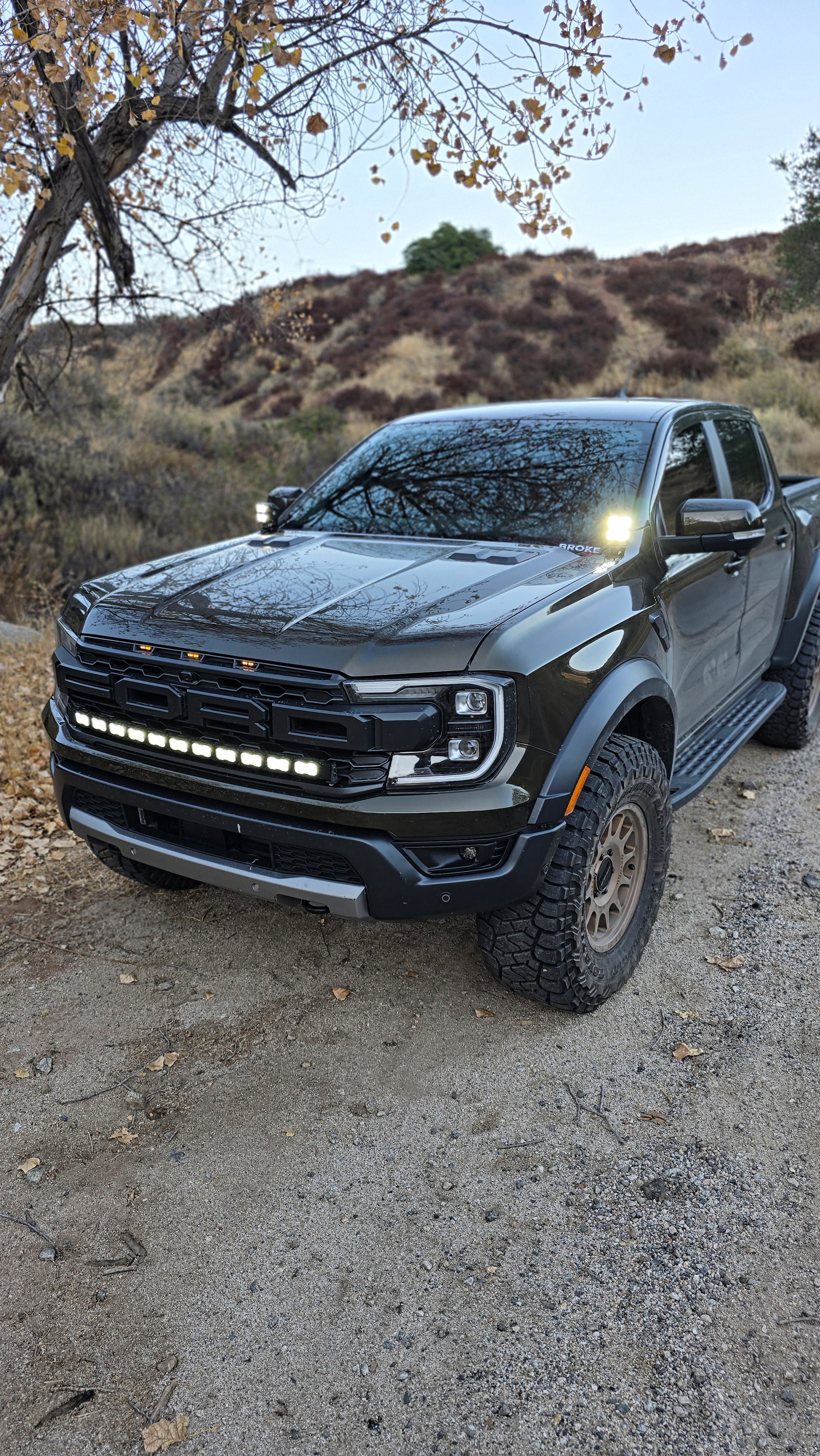 Ranger Raptor ditch lights installed on a dark Ford Ranger Raptor 2024+ with dual white and amber DRL glow in off-road terrain