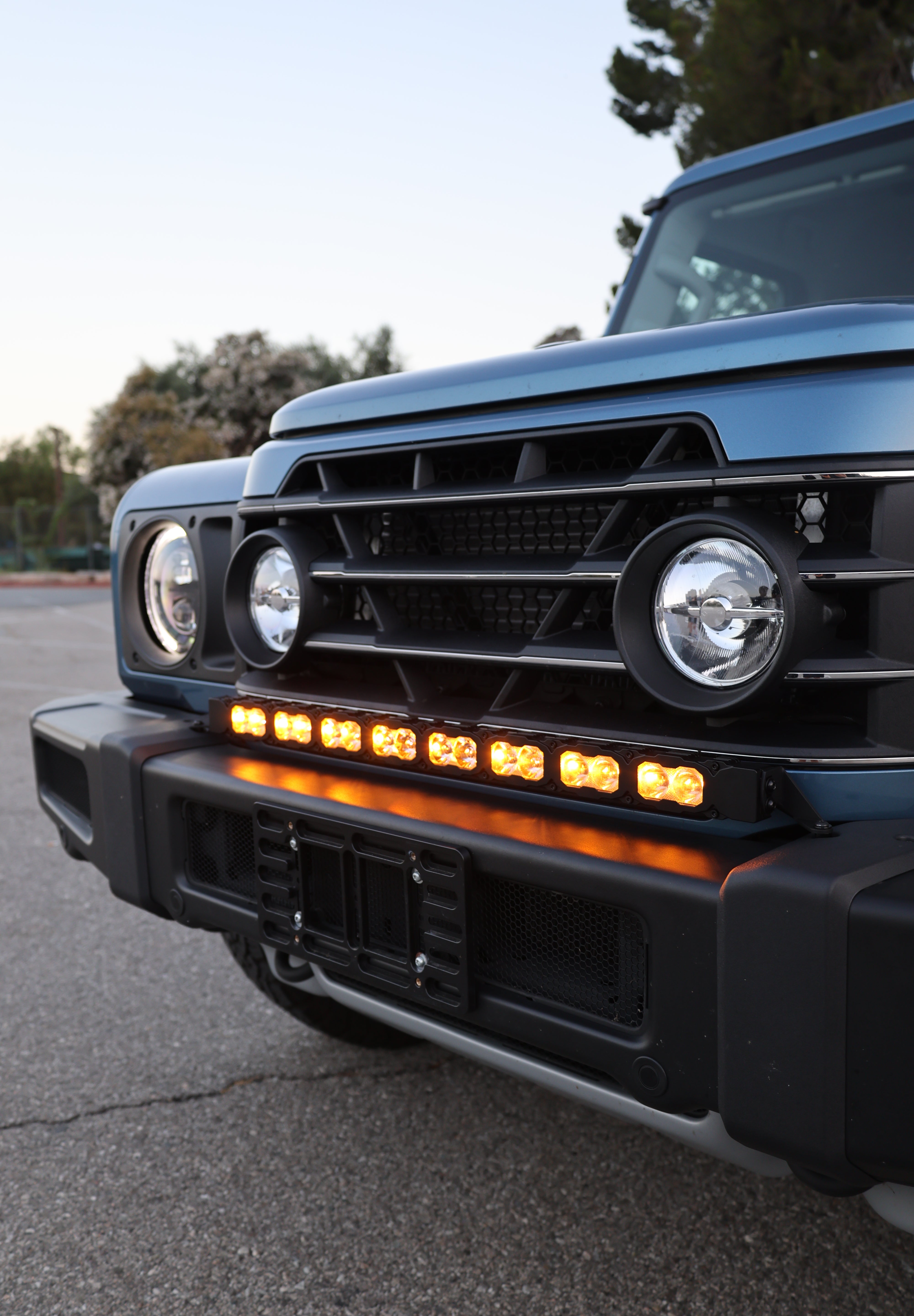 Ineos Grenadier 30in light bar lit in yellow across the front bumper at dusk, off-road driving lights