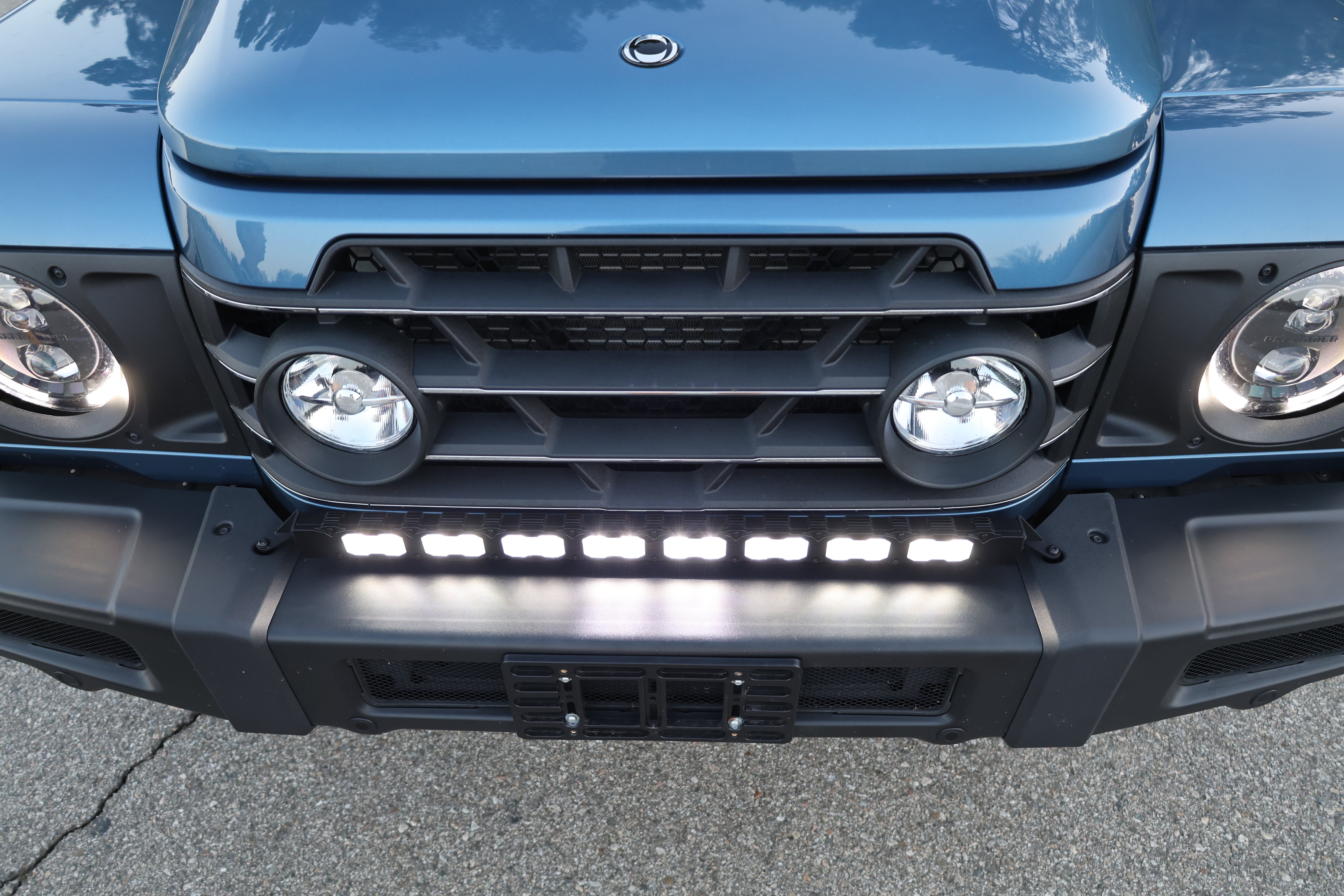 Light-blue 2024+ Ineos Grenadier front corner with 30in bumper light bar and round headlight, daylight