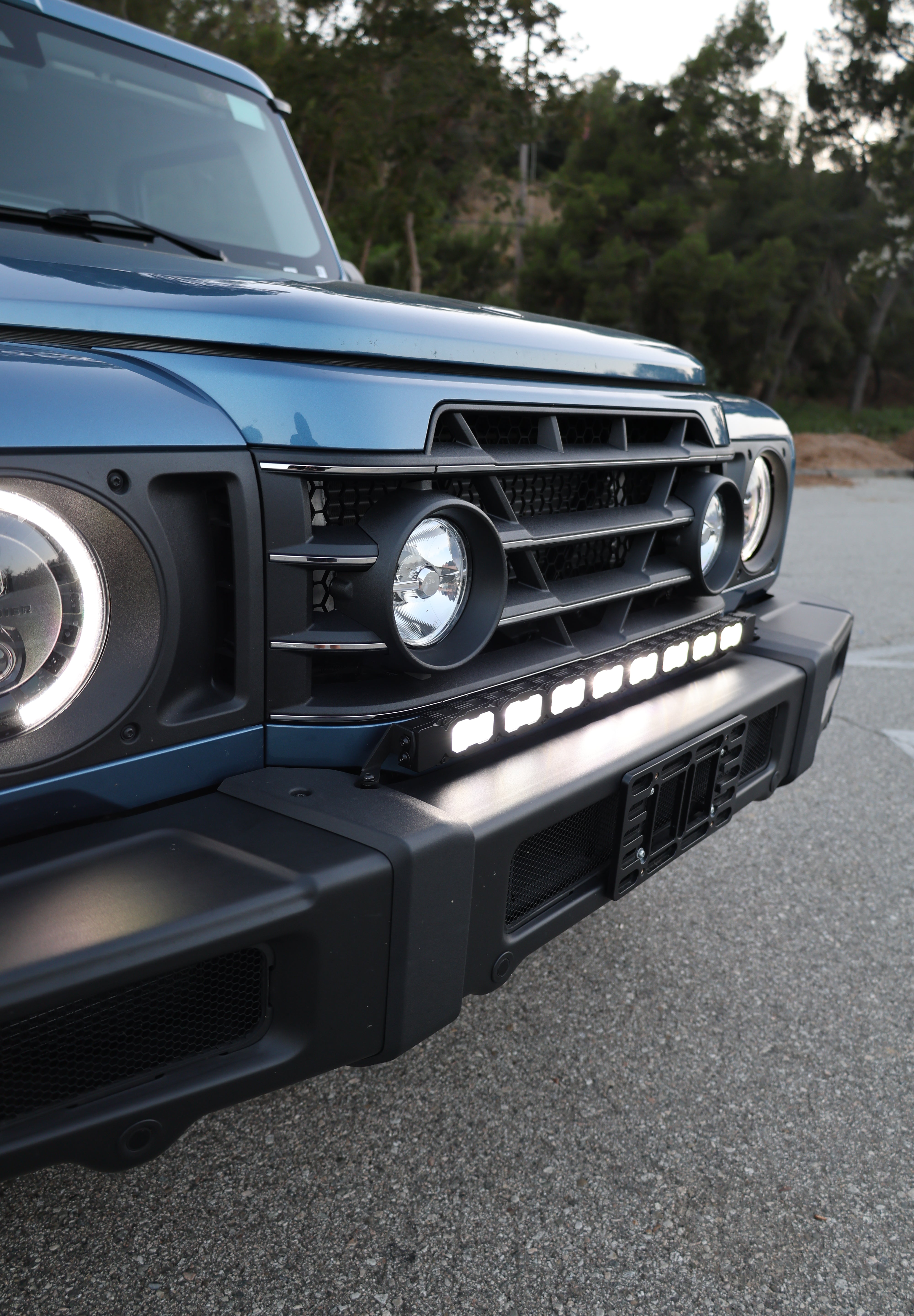 Light-blue Ineos Grenadier hood and windshield with 30in bumper light bar mounted below, daylight