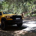 Yellow RAM 1500 with front RAM TRX Light bar slim 23in curved LED installed between grille and bumper on forest road