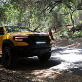 Yellow RAM 1500 with front RAM TRX Light bar slim 23in curved LED installed between grille and bumper on forest road