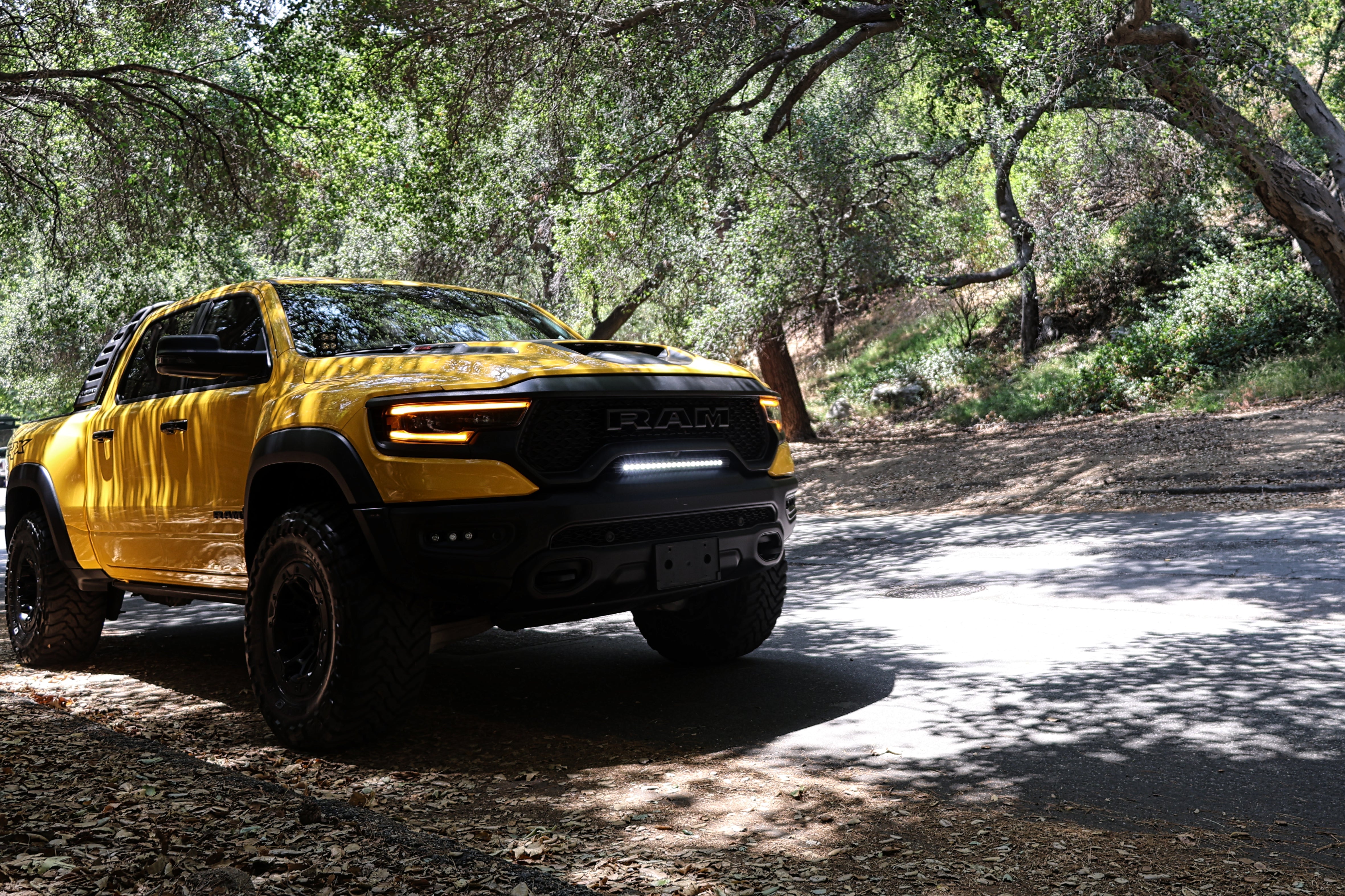 Yellow RAM 1500 with front RAM TRX Light bar slim 23in curved LED installed between grille and bumper on forest road