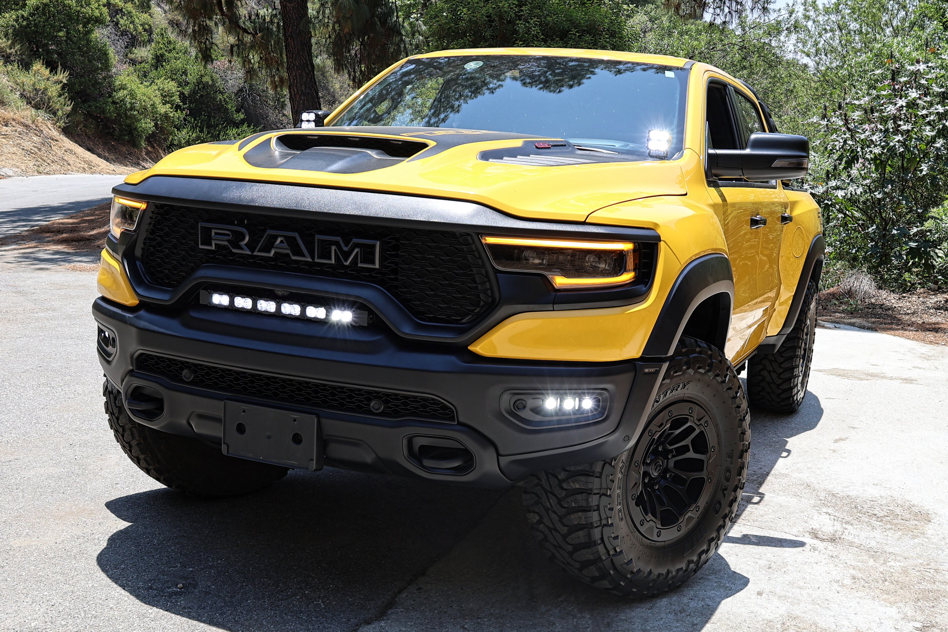 Yellow 2019-2024 RAM 1500 TRX with fog light kit installed, three white LED pods lit in the front bumper, front three-quarter view