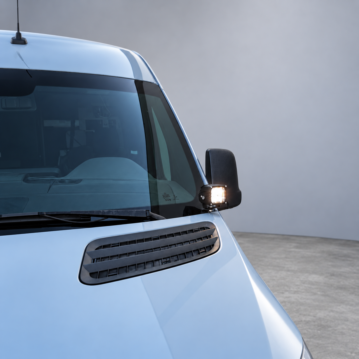 Close-up of a 2019+ Mercedes Sprinter ditch light LED pod lit white beside the windshield and side mirror