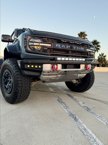 front of ford bronco raptor with white led light bar on top of bumper and fog lights off roading