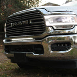 Close-up of the 30in light bar lit white below the chrome grille of a white 2019-2024 RAM 3500 dually, showing bracket fitment
