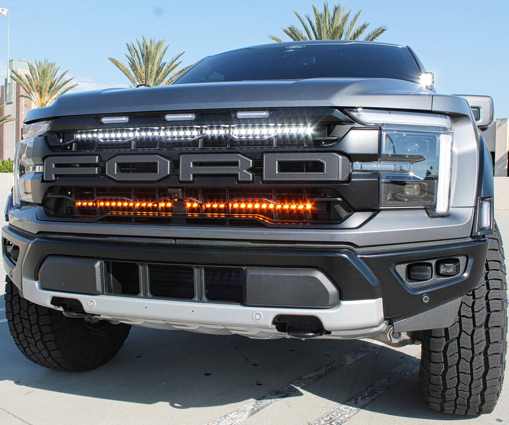 gray 2024 ford raptor with LED light bars behind the grille white and amber for off roading