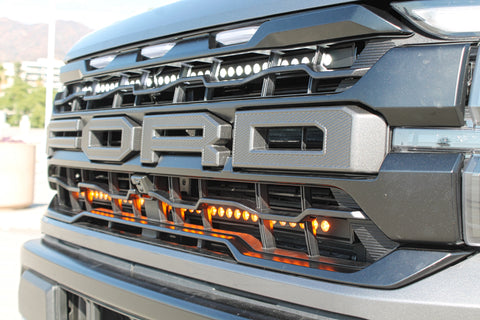 up close grille of gray 2024 ford raptor with LED light bars behind the grille white and amber for off roading