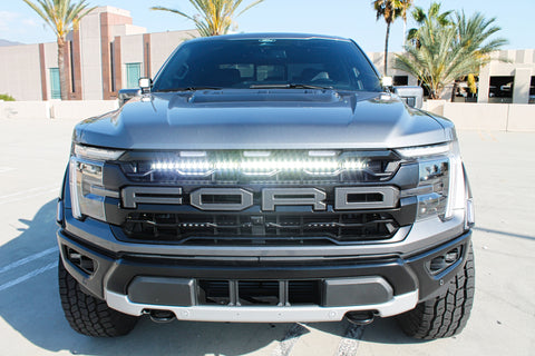 gray 2024 ford raptor with white LED light bar behind the grille and white light ditch lights for off roading