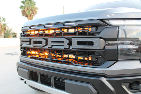 front view grille of gray 2024 ford raptor gen 3 with 2 light bars behind the grille with amber backglow on