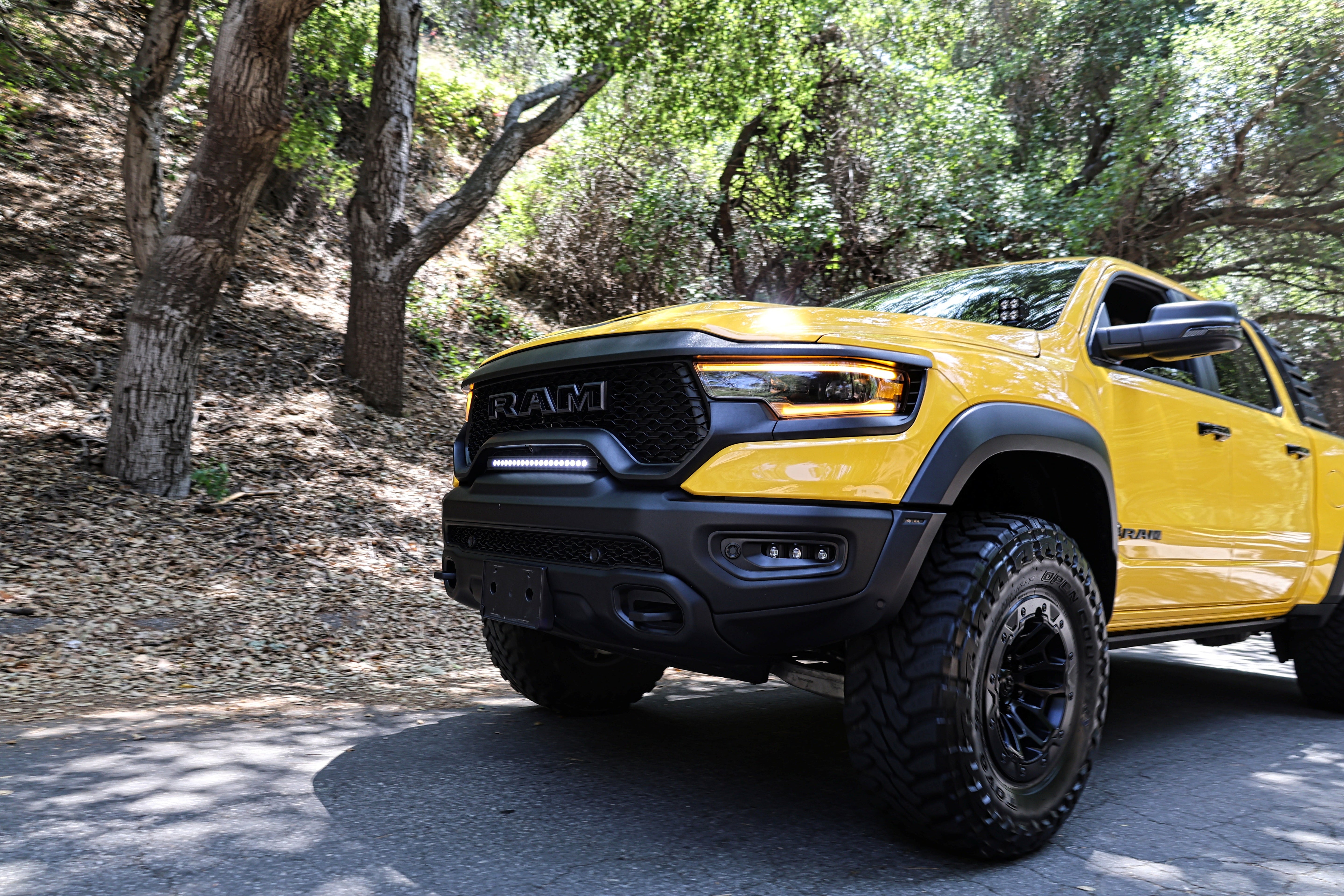 RAM TRX Light bar slim 23in installed on yellow 2021-2024 RAM 1500 TRX between grille and bumper on forest road