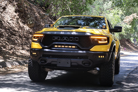 RAM TRX Lightbar 23in PRO installed on yellow 2021-2024 RAM 1500 TRX front grille and bumper opening on forest road