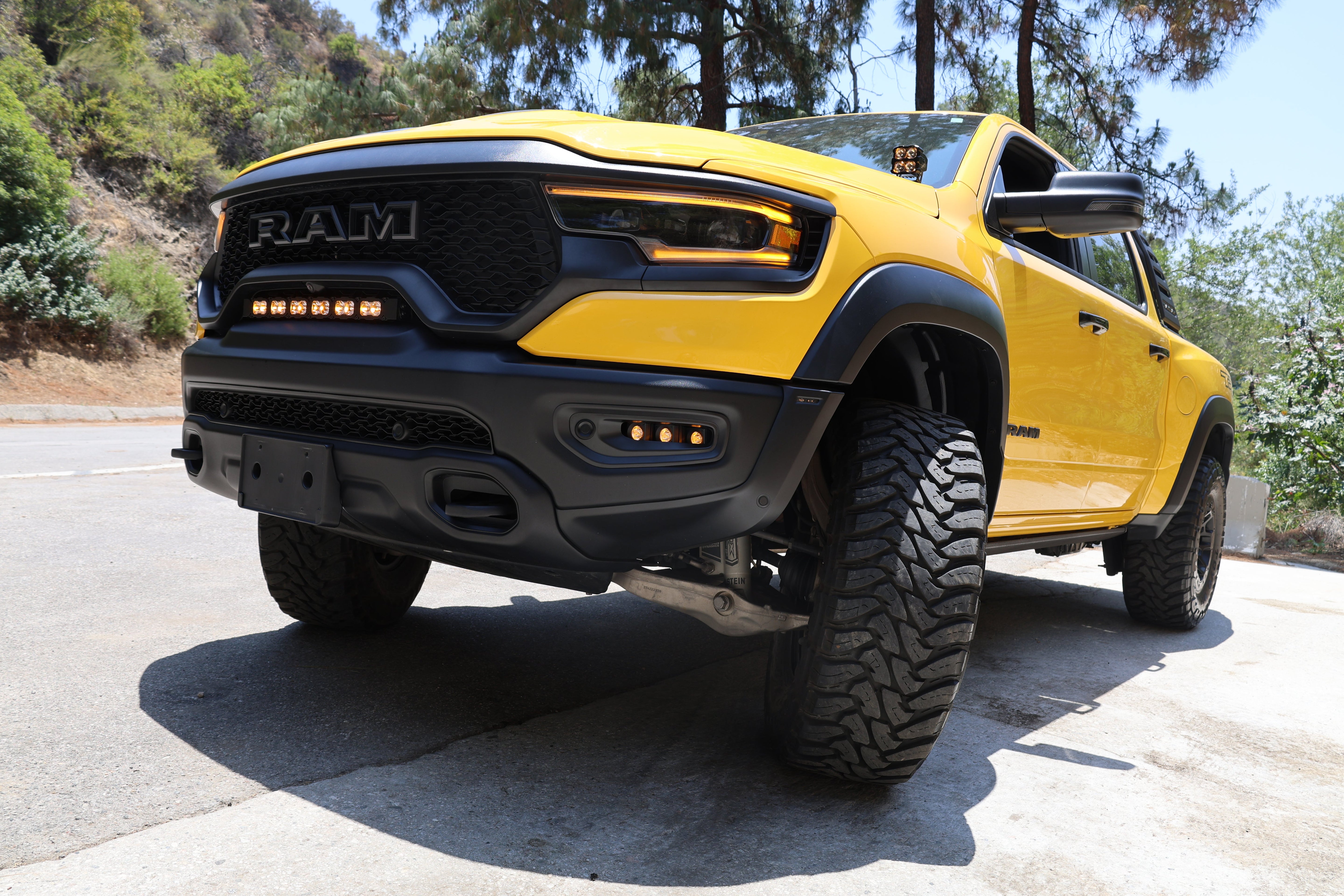 RAM TRX Lightbar 23in PRO installed on yellow RAM 1500 TRX 2021-2024 between grille and bumper on mountain road
