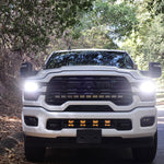 2025+ RAM 2500 Light kit lower grille pods with bright LED lights installed on white RAM 2500 truck front view on forest road
