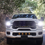 2025+ RAM 2500 Light kit lower grille pods with bright LED lights installed on white RAM 2500 truck front view on forest road