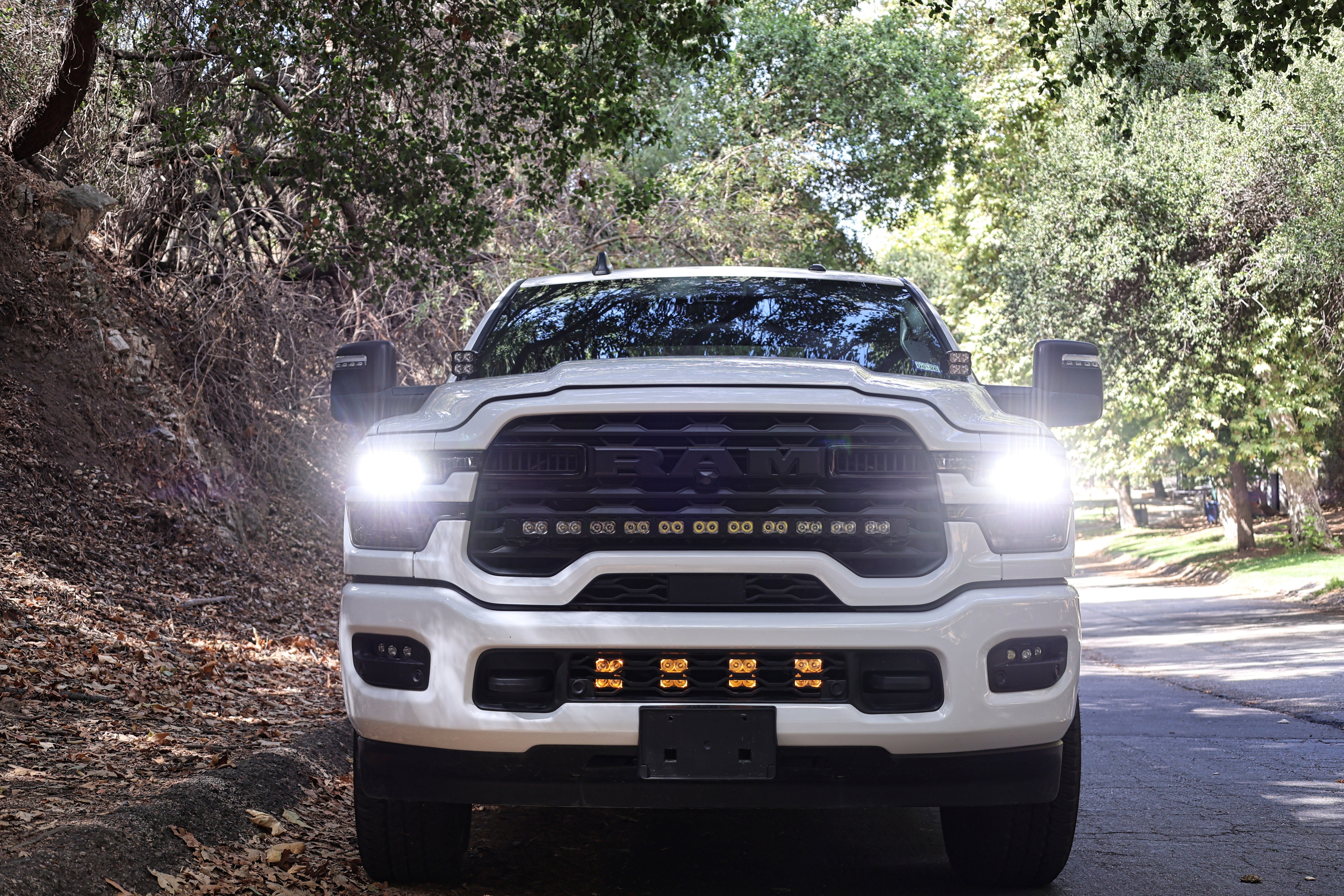 2025+ RAM 2500 Light kit lower grille pods with bright LED lights installed on white RAM 2500 truck front view on forest road