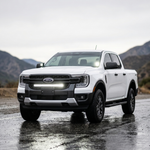 White Ford Ranger with a 30-inch SLIM LED light bar in the front grille, parked on a wet road with mountains behind