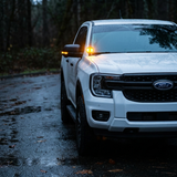 White Ford Ranger with the LED ditch lights on, parked on a wet forest road