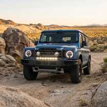 Blue 2024+ Ineos Grenadier parked among desert boulders at sunset with 30in bumper light bar, off-road setup