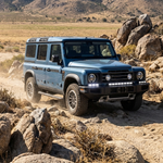 Blue Ineos Grenadier climbing desert rocks with XL 30in-plus-12in light bar kit lit white, off-road action