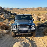2024+ Ineos Grenadier head-on in the desert with XL light bar kit lit white, 30in center bar and two 12in extensions