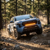 2024+ Toyota Tacoma with 30-inch amber LED off-road light bar mounted on front grille, driving up a rocky forest trail
