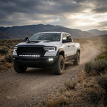 White 2025+ RAM 1500 Rebel driving a desert dirt road with the fog light kit's white LED pods lit in the front bumper, front three-quarter view