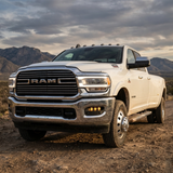 White 2019-2024 RAM 3500 dually parked in the desert with the fog light kit running amber DRL in the front bumper, front three-quarter view