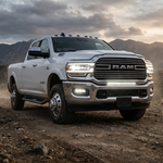 White 2019-2024 RAM 2500 on a desert trail at sunset with the 30in light bar lit white in the lower grille, front three-quarter view