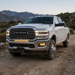White 2019-2024 RAM 3500 dually on a desert trail at dusk with the fog light kit running amber DRL in the chrome front bumper