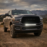 Gray 2019-2024 RAM 2500 on a mountain dirt trail with the 30in light bar lit white in the lower grille, front three-quarter view