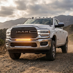 White 2019-2024 RAM 2500 on a dirt road with the 30in light bar running amber in the lower grille, front three-quarter view