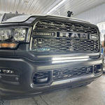 Close-up of the 30in light bar lit white in the lower grille of a gray 2019-2024 RAM 2500 in a shop