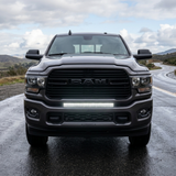 Gray 2019-2024 RAM 2500 straight-on front view on a wet road with the 30in light bar lit white in the lower grille