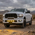 2025+ RAM 2500 lower grille pods with yellow LED lights lit, white truck in the desert at dusk, front three-quarter view
