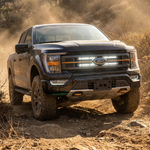Black 2021-2023 Ford F150 Tremor kicking up dust with dual white 30in LED light bars lit behind the grille