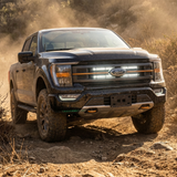 Black 2021-2023 Ford F150 Tremor kicking up dust with dual white 30in LED light bars lit behind the grille