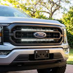 Close-up of a 2021-2023 Ford F150 grille with dual white 30in LED light bars lit above and below the Ford emblem