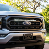 Close-up of a 2021-2023 Ford F150 grille with a single white 30in LED light bar lit above the Ford emblem