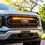 Close-up of a 2021-2023 Ford F150 grille with a single amber 30in LED light bar lit above the Ford emblem