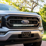 Close-up of a 2021-2023 Ford F150 grille with a single white 30in LED light bar lit below the Ford emblem