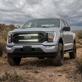 Silver 2021-2023 Ford F150 on a dirt trail with dual white 30in LED light bars lit behind the grille