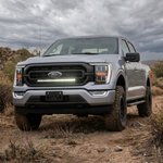 Silver 2021-2023 Ford F150 on a dirt trail with a single white 30in LED light bar lit in the lower grille