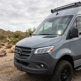 2019+ Mercedes Sprinter 4x4 van in the desert with a PRO ditch light lit white at the mirror base and a light bar on the grille
