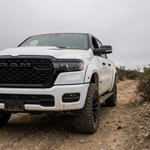 White 2026 RAM 1500 HEMI with 40in curved LED light bar SLIM, front three-quarter view on a dirt trail