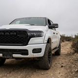 White 2026 RAM 1500 HEMI with 40in curved LED light bar SLIM, front three-quarter view on a dirt trail